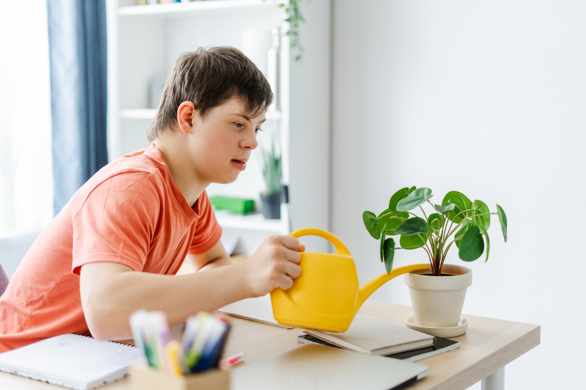 Smiling, happy teenager with down syndrome watering plant on desk at home