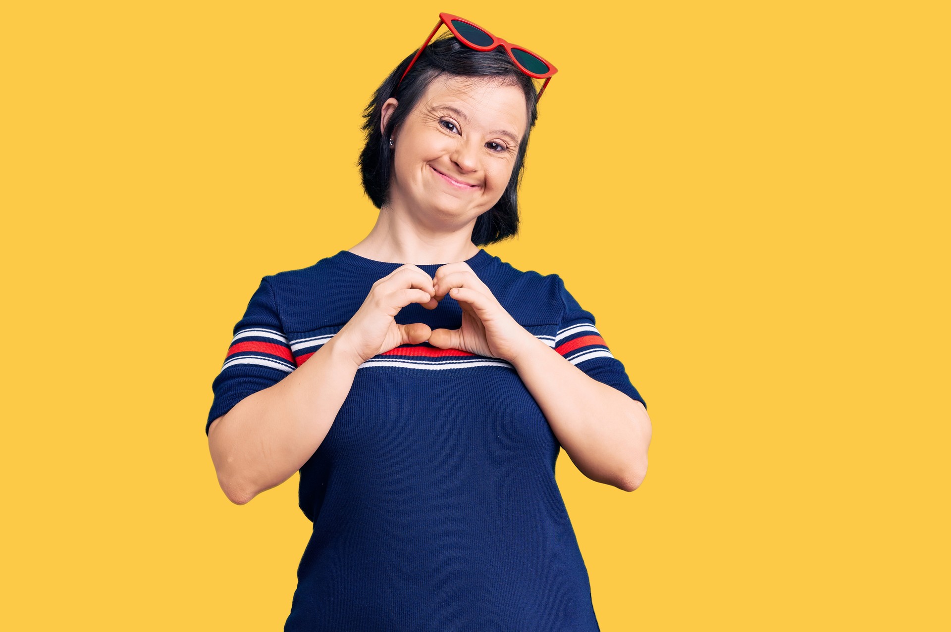 Brunette woman with down syndrome wearing casual clothes smiling in love showing heart symbol and shape with hands. romantic concept.