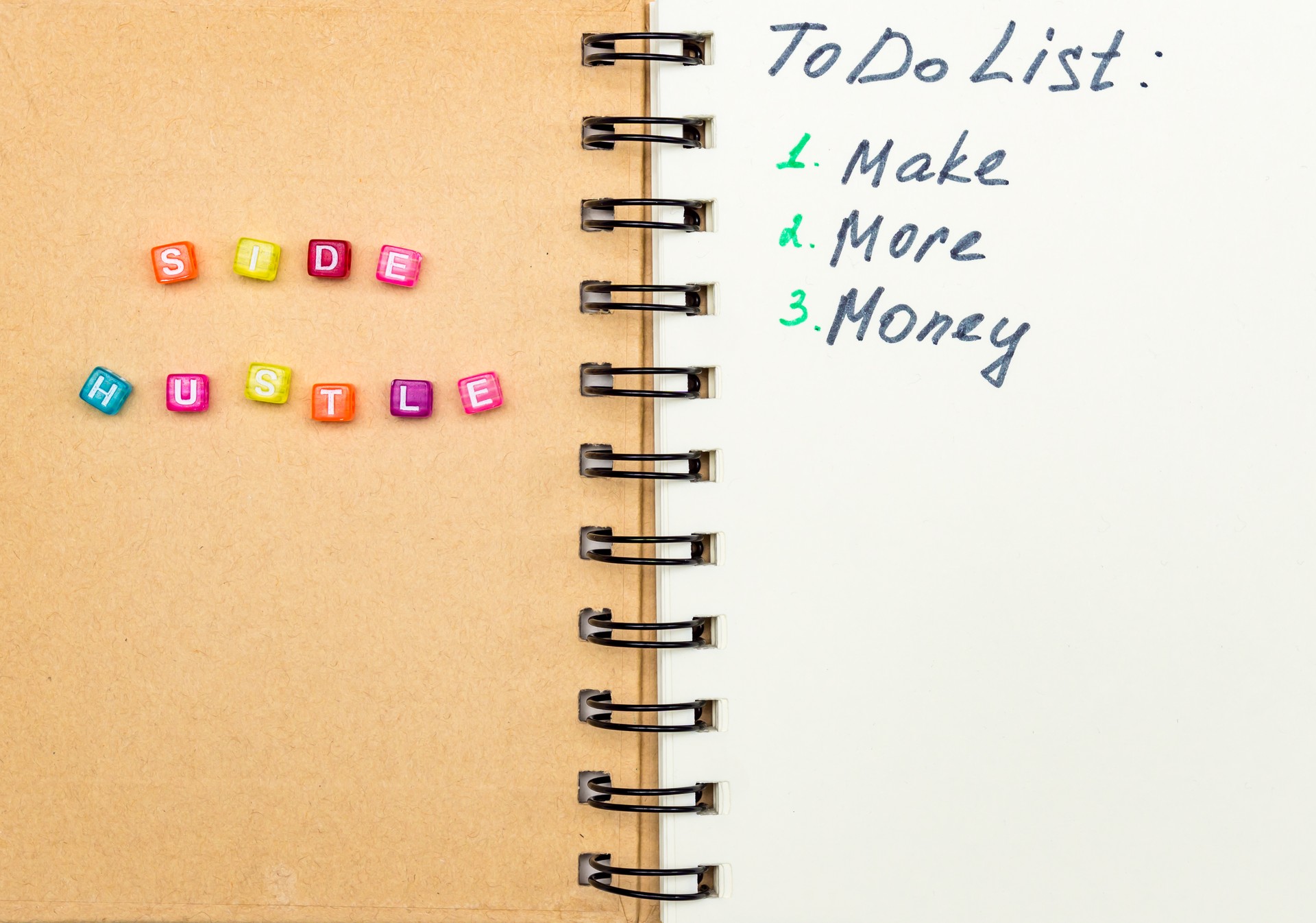 Side Hustle words made form multicolored square beads on spiral notebook cover. Concept image of passive income